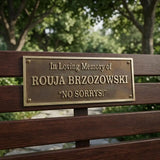 cast bronze bench plaque dilled on Wooden bench with text honoring Rouja Brzozowski and her quote 'No Sorrys!'.