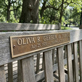 Wooden bench with a brass bench memorial plaque bearing a name and dates in a park setting