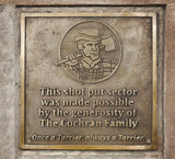 Bronze plaque with a logo of a person holding an axe and engraved text on a stone wall.