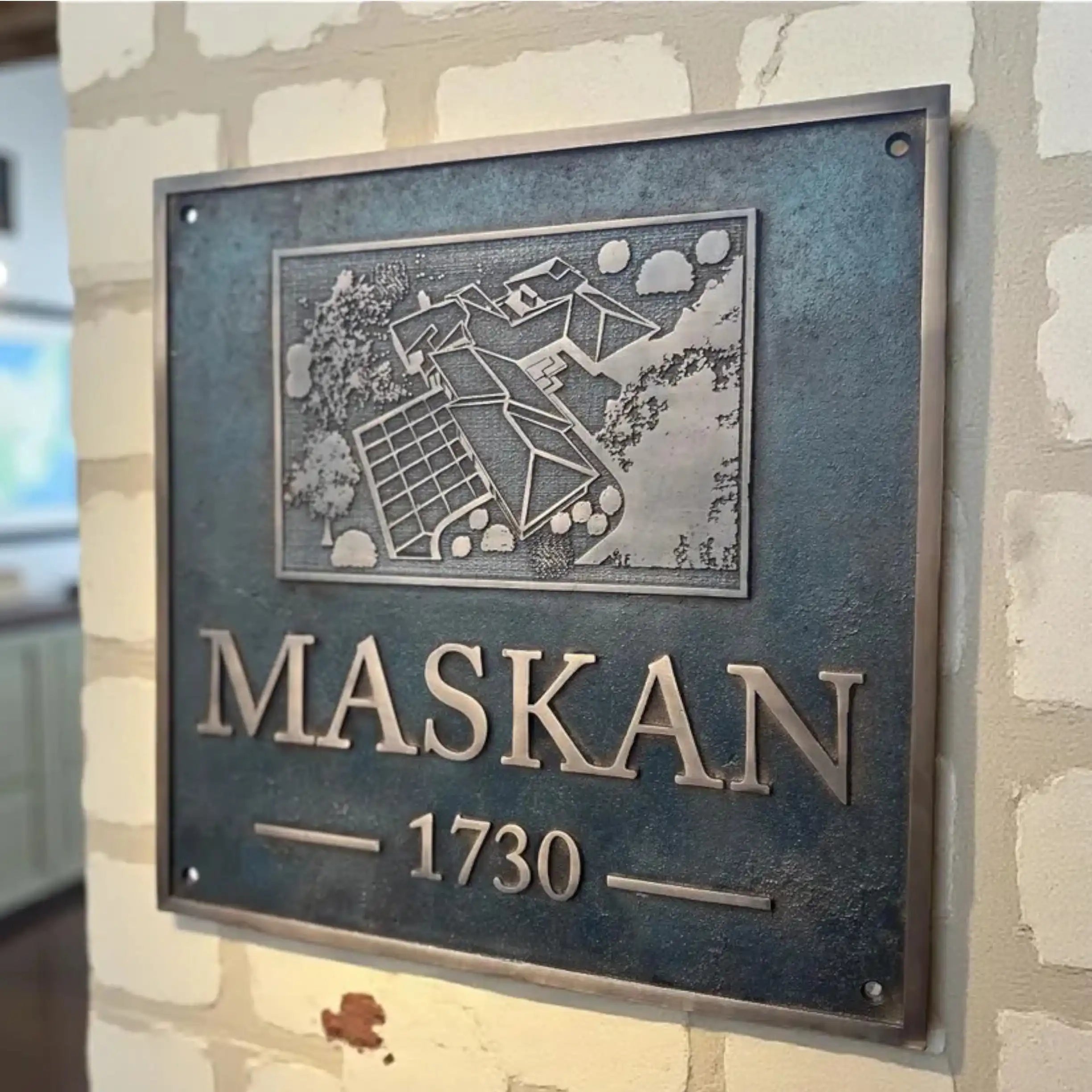 Metal plaque with 'MASKAN 1730' on a textured wall
