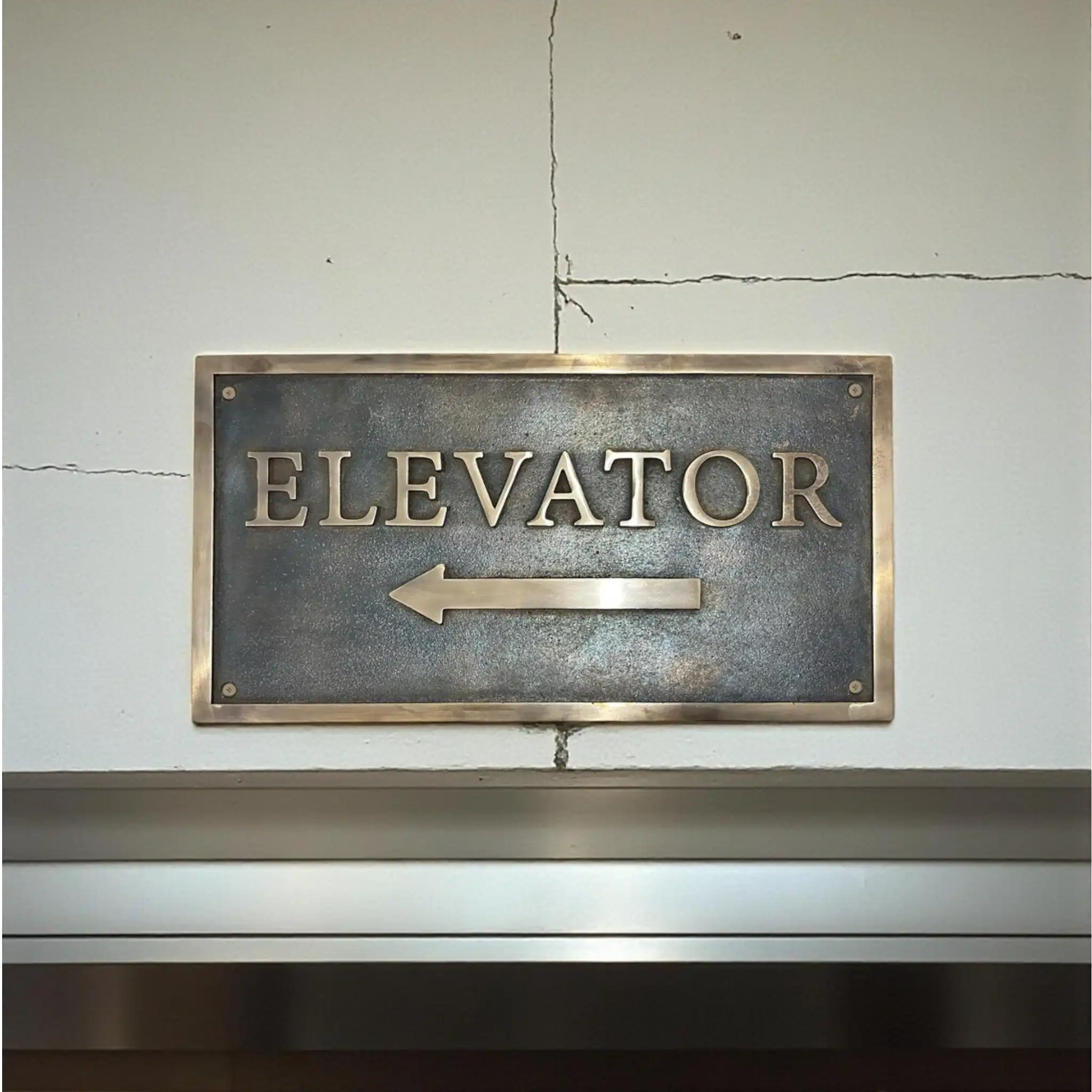 Bronze Address sign - Bronze 'ELEVATOR' sign with arrow on a textured wall.