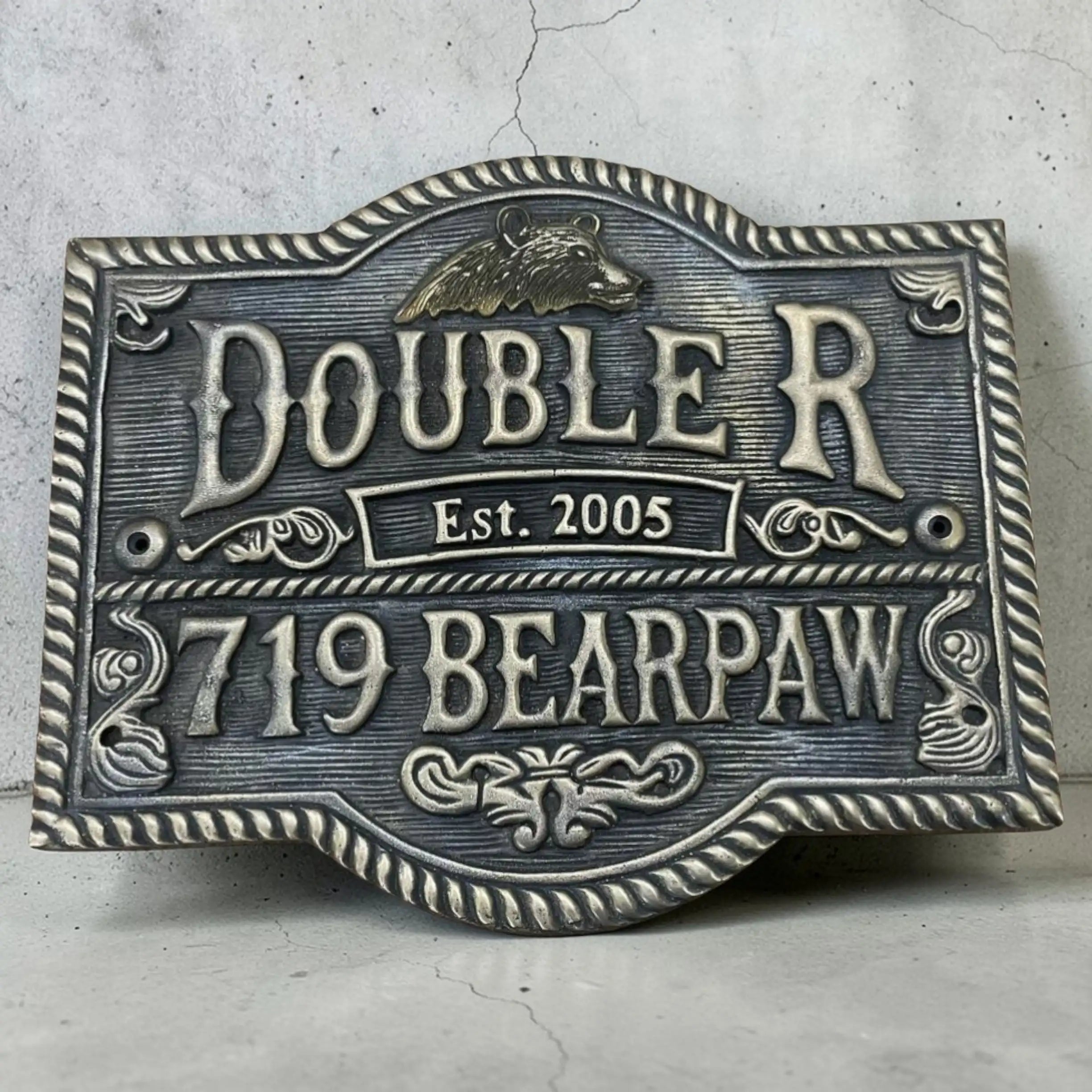 Decorative bronze sign with 'Doublerr' and '719 Bearpaw' text on a textured surface