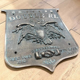 Bronze plaque with an eagle emblem and engraved text on a wooden surface