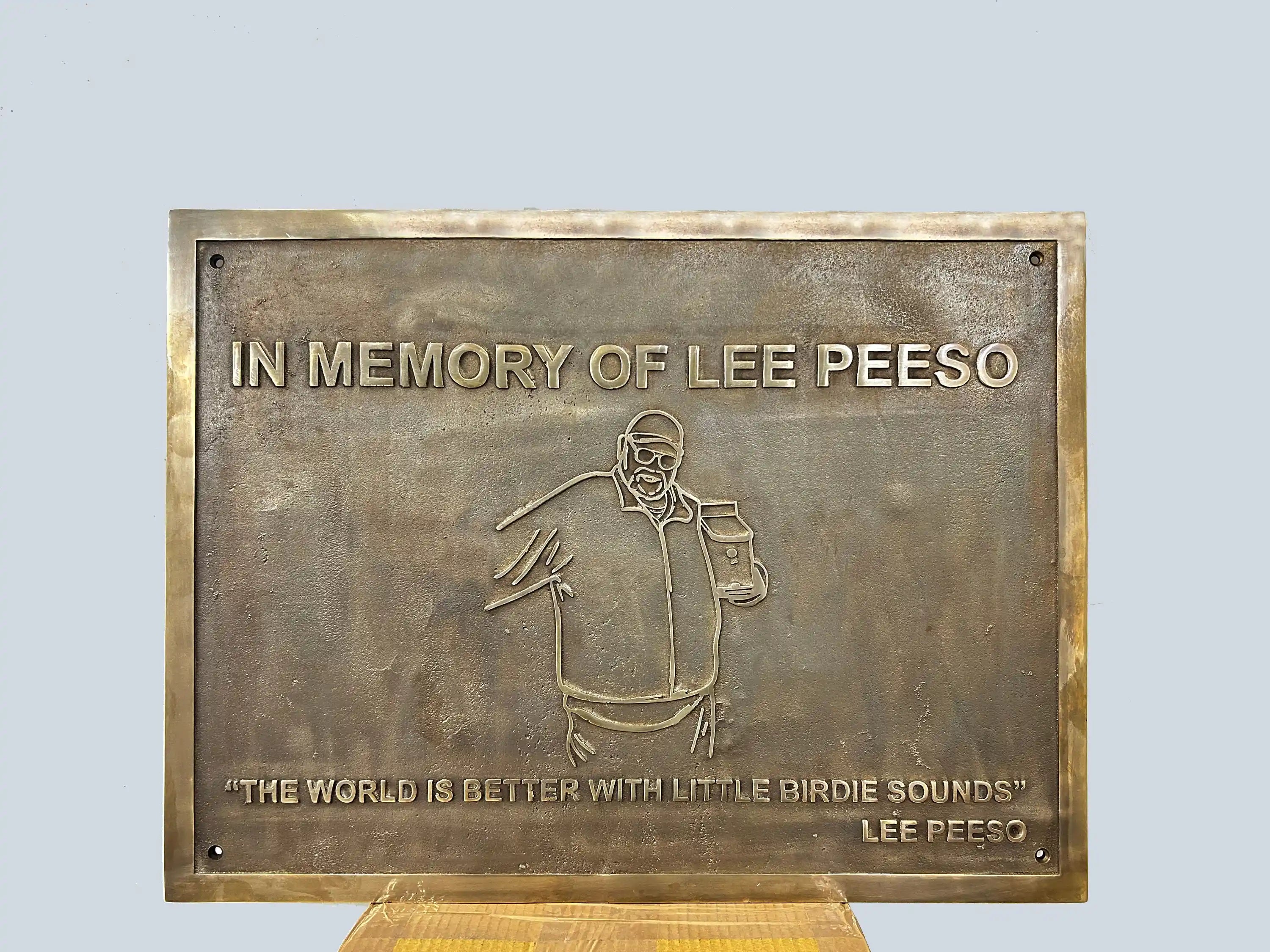Bronze plaque with engraved text and illustration of a person, on a light gray background