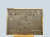Bronze plaque with engraved text and illustration of a person, on a light gray background