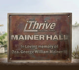 Metal plaque with 'iThrive Christian Church' and 'Mainer Hall' engraved on a blurred natural background