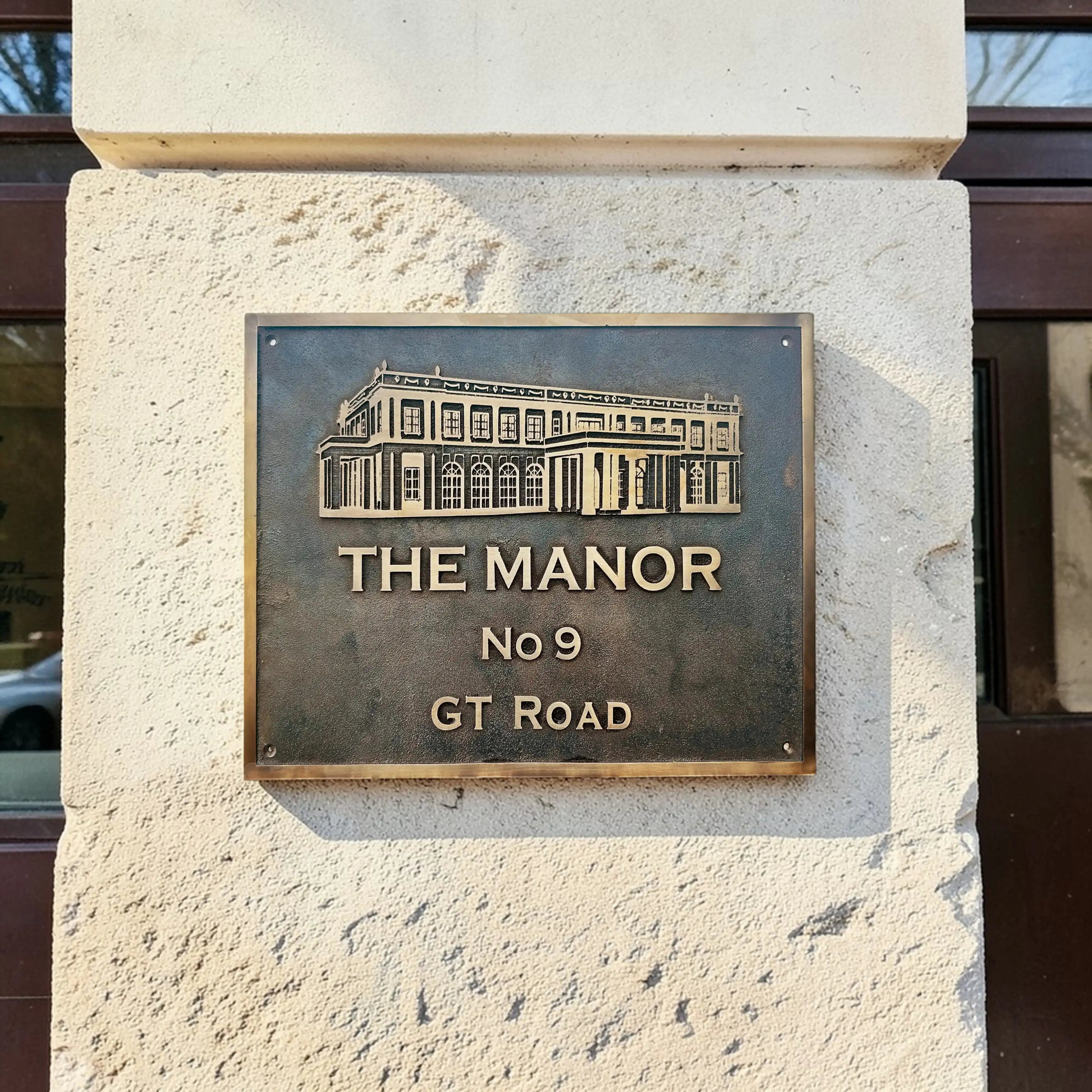 Bronze plaque with 'The Manor No 9 GT Road' on a stone wall