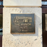 Bronze plaque with 'The Manor No 9 GT Road' on a stone wall