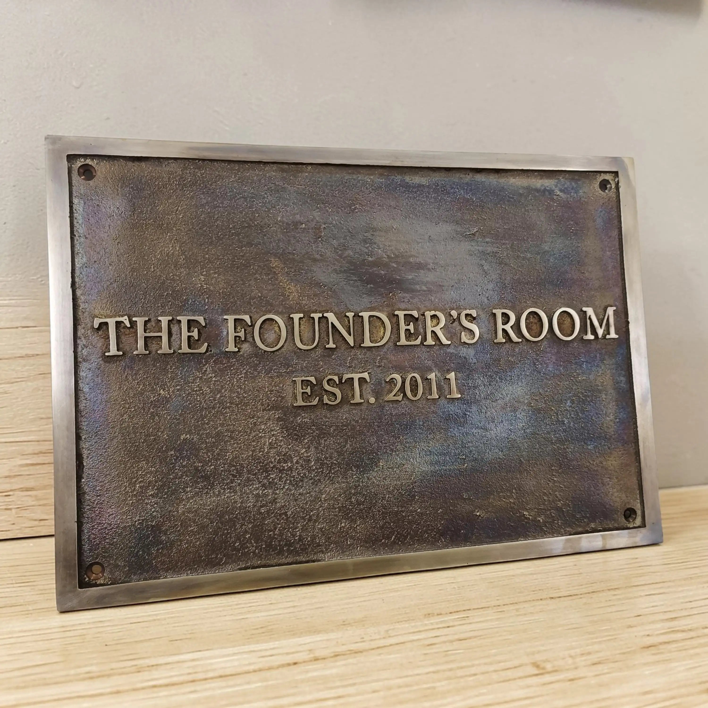 Bronze plaque with 'The Founder's Room EST. 2011' text on a wooden surface.