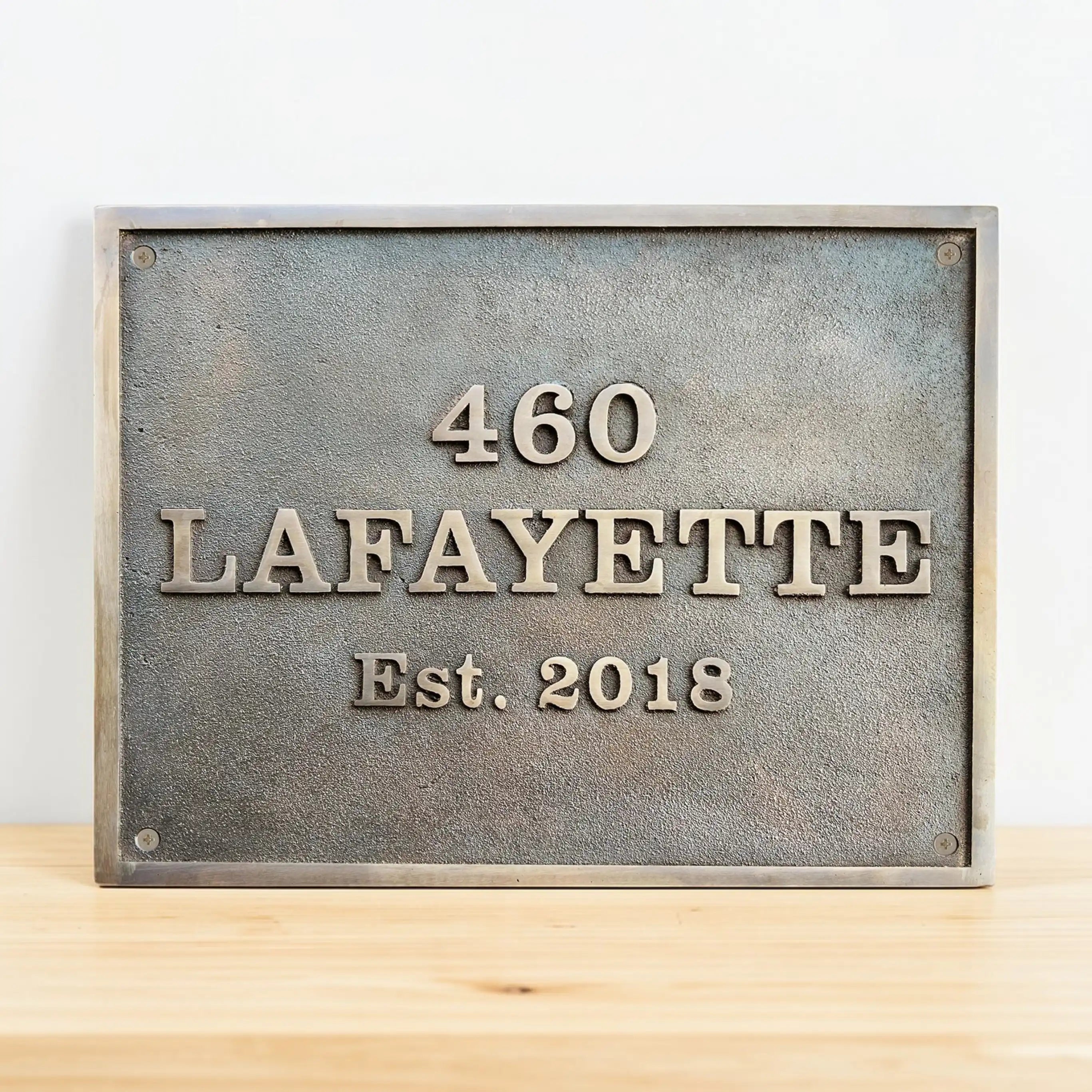 Bronze metal plaque with engraved text '460 Lafayette Est. 2018' on a wooden surface.