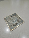 Decorative bronze metal plaque with emblem on a gray surface