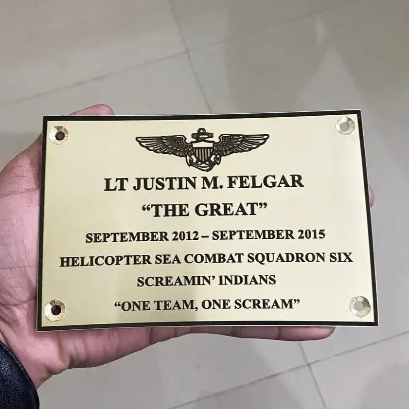 Brass engraving Plaque held by a hand with text and insignia on a beige background