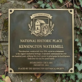 Plaque commemorating the Kensington Watermill, a National Historic Place, on a stone wall with ivy.