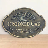 Bronze sign with 'Crooked Oak' and tree design on a wooden surface.