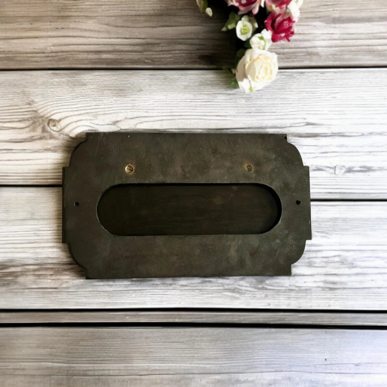 Rectangular metal letterbox on a wooden surface with flowers in the corner