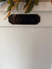 Decorative metal letter box sign on a white wall with green leaves above.