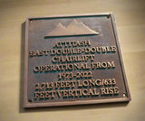Metal plaque with engraved text about a chairlift on a wooden background
