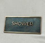Rectangular metal sign with 'SHOWER' text on a gray background