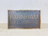 Metal sign with 'Farnham Eye Care' text on a white background