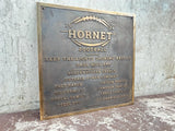 Bronze plaque with 'Hornet Football' text and sponsor names on a textured wall background