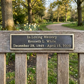 Bench Memorial plaque for Kenneth L. White in a park setting with trees and flowers.