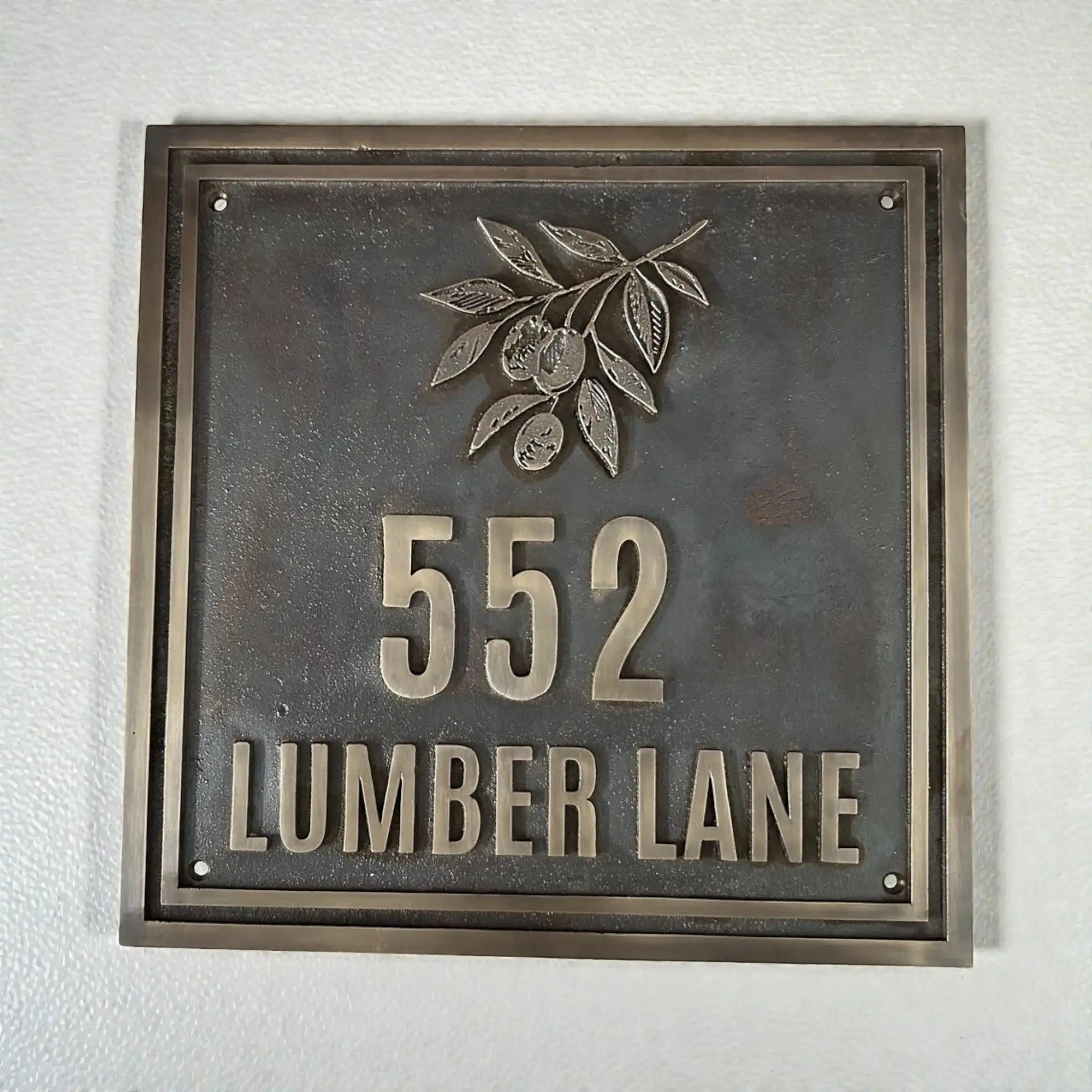 Cast bronze house number plaque - Metallic house number sign with '552 LUMBER LANE' on a textured wall.