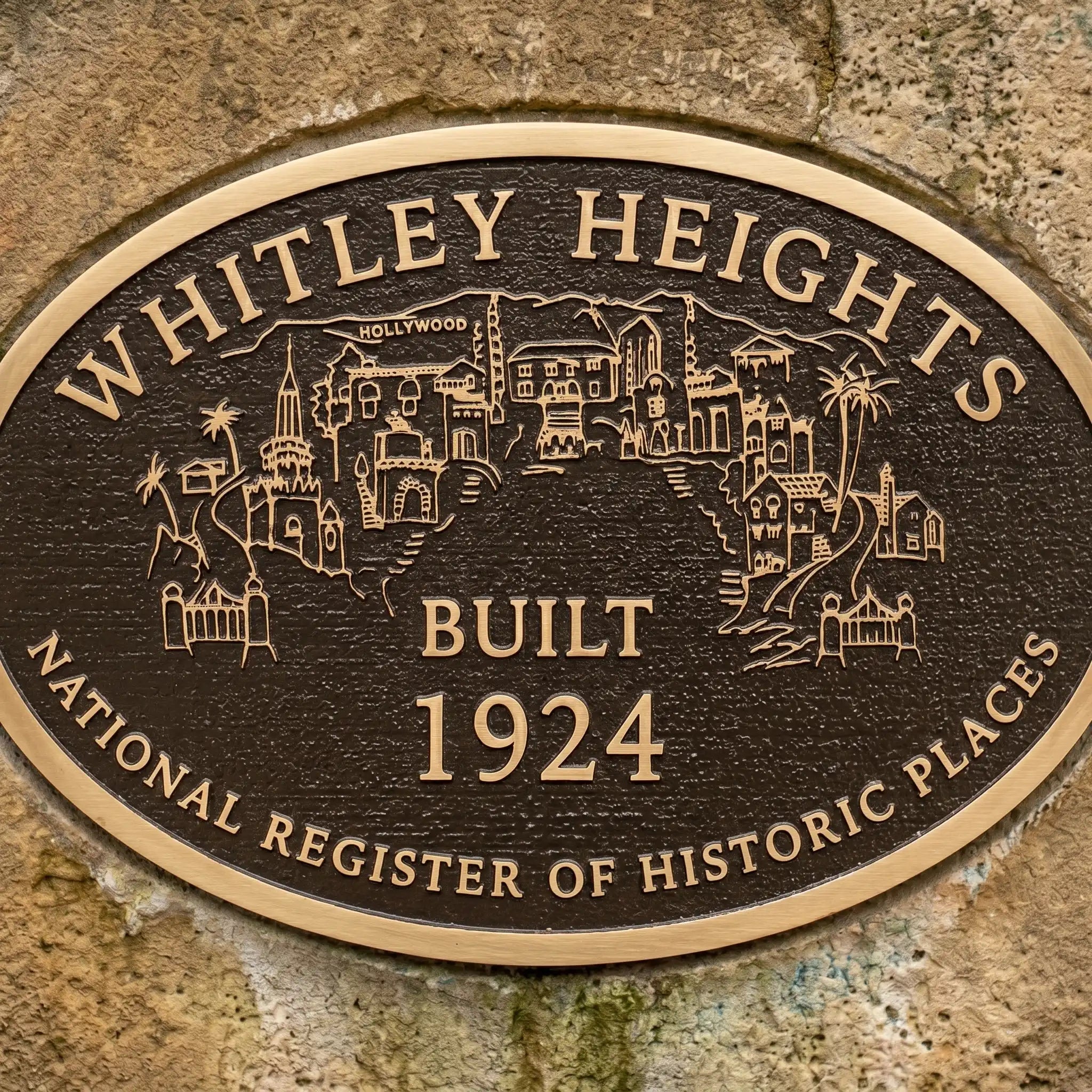 Personalized bronze memorial plaque with raised lettering with 'Whitley Heights' text and building illustrations on a stone wall.