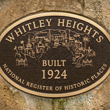 Personalized bronze memorial plaque with raised lettering with 'Whitley Heights' text and building illustrations on a stone wall.