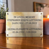 Memorial plaque with names and dates on a wooden surface with a candle and plant in the background