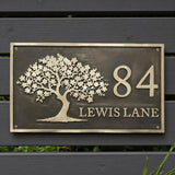 Bronze house number sign with tree design on a wooden background