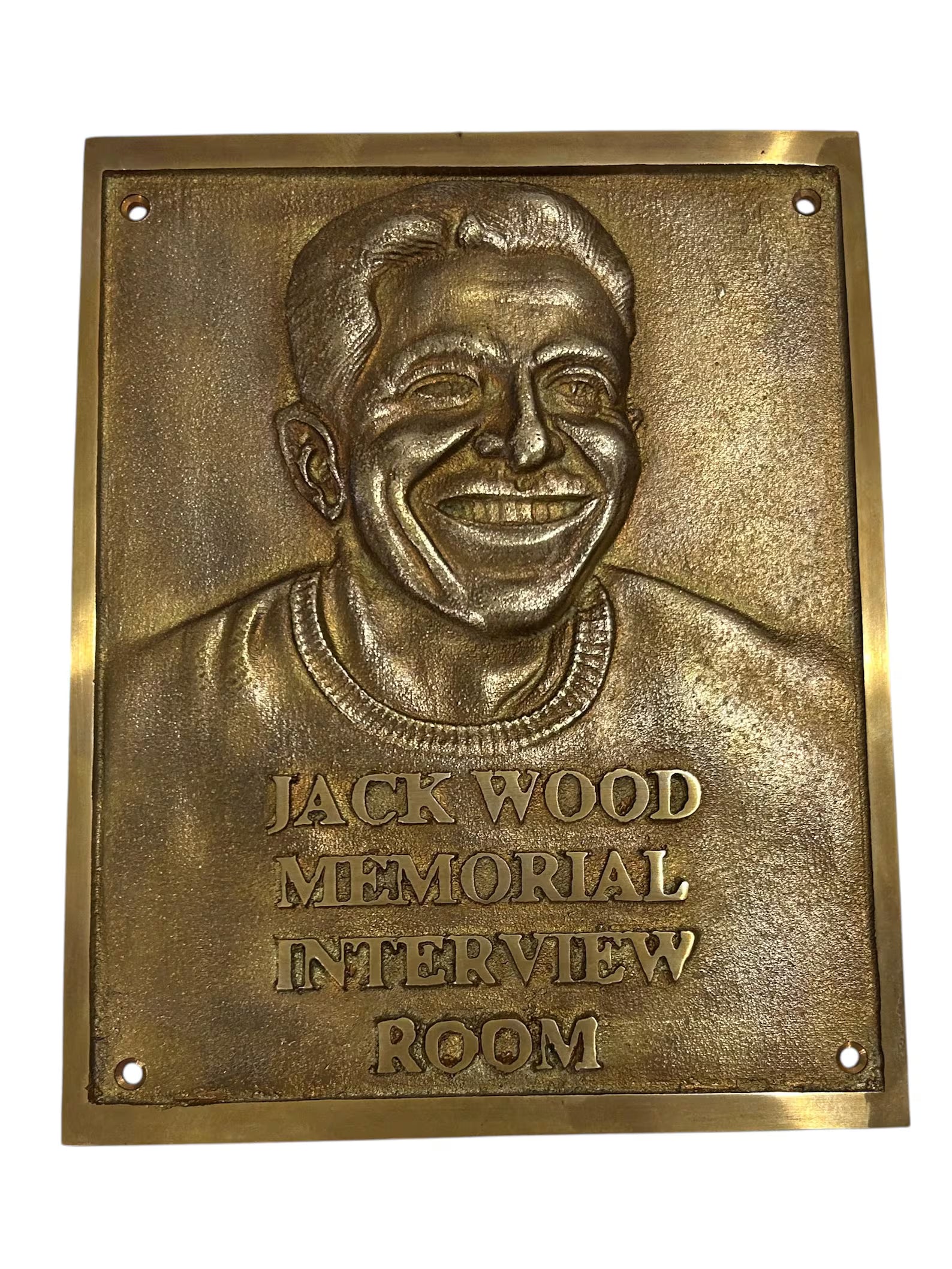 Bronze plaque with a smiling face and engraved text 'Jack Wood Memorial Interview Room' on a white background