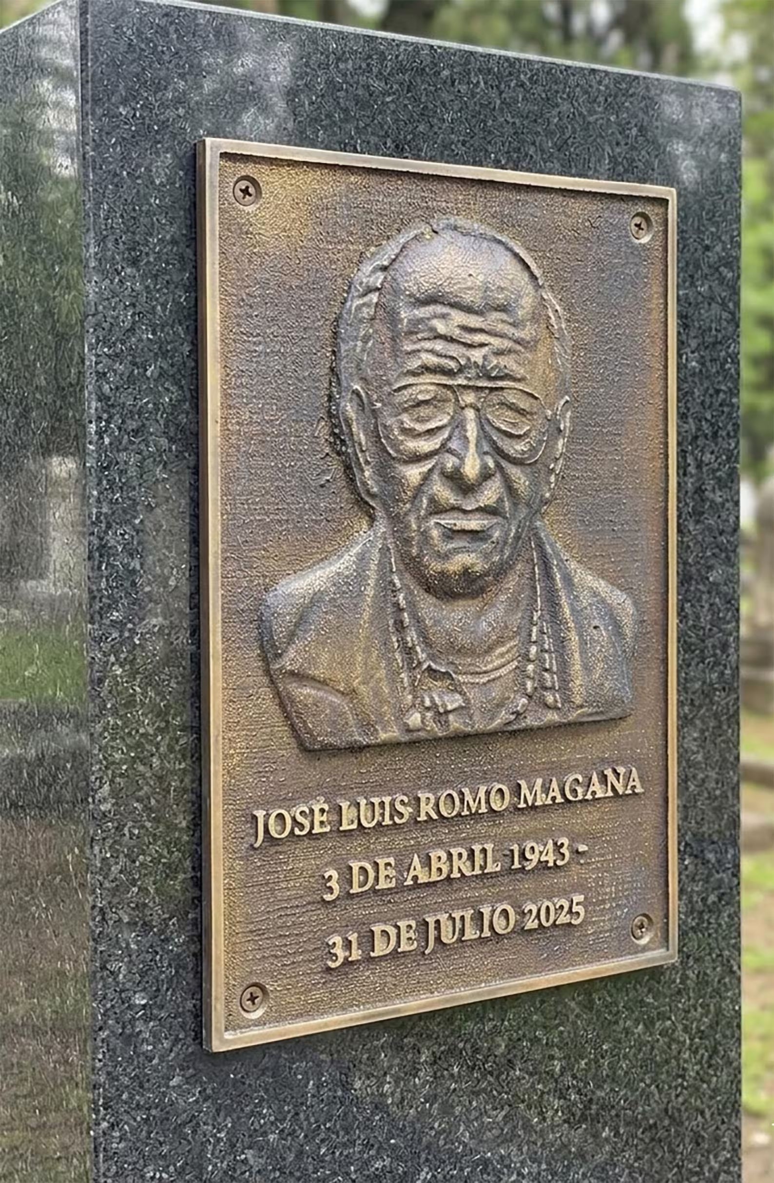 Bronze plaque with a portrait and dates on a stone wall in a cemetery