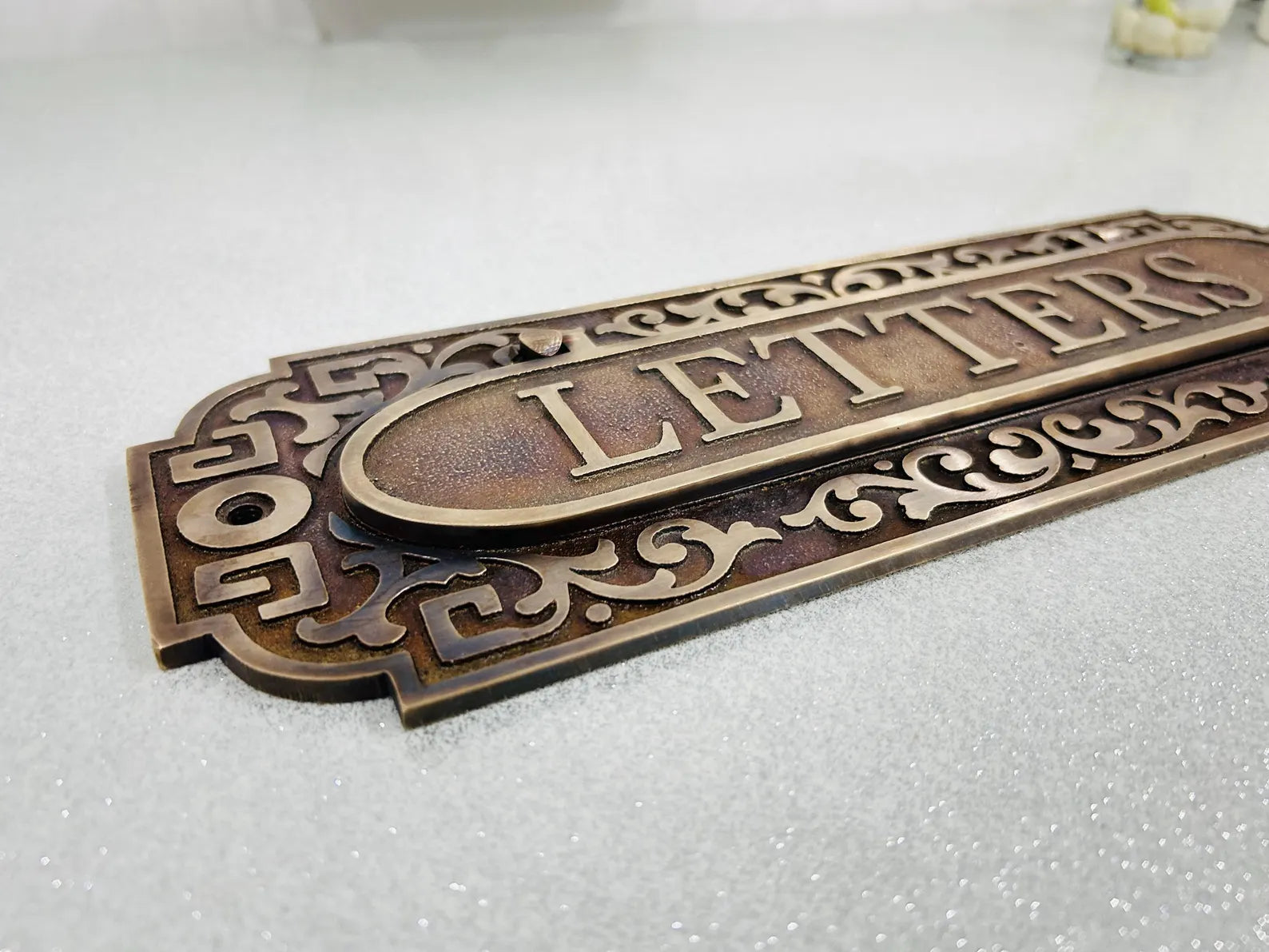 Decorative metal letter box sign with ornate design on a white background