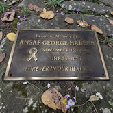 Bronze plaque commemorating Ansaaf George Habeeb with a gold ribbon on a stone surface with leaves and flowers.
