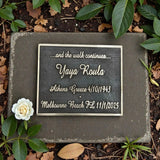 Memorial plaque with engraved text on a stone slab surrounded by plants and leaves.