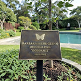 Memorial plaque for Barbara Irene Glenn at a pool named 'Goddamit' with a garden and pool in the background.