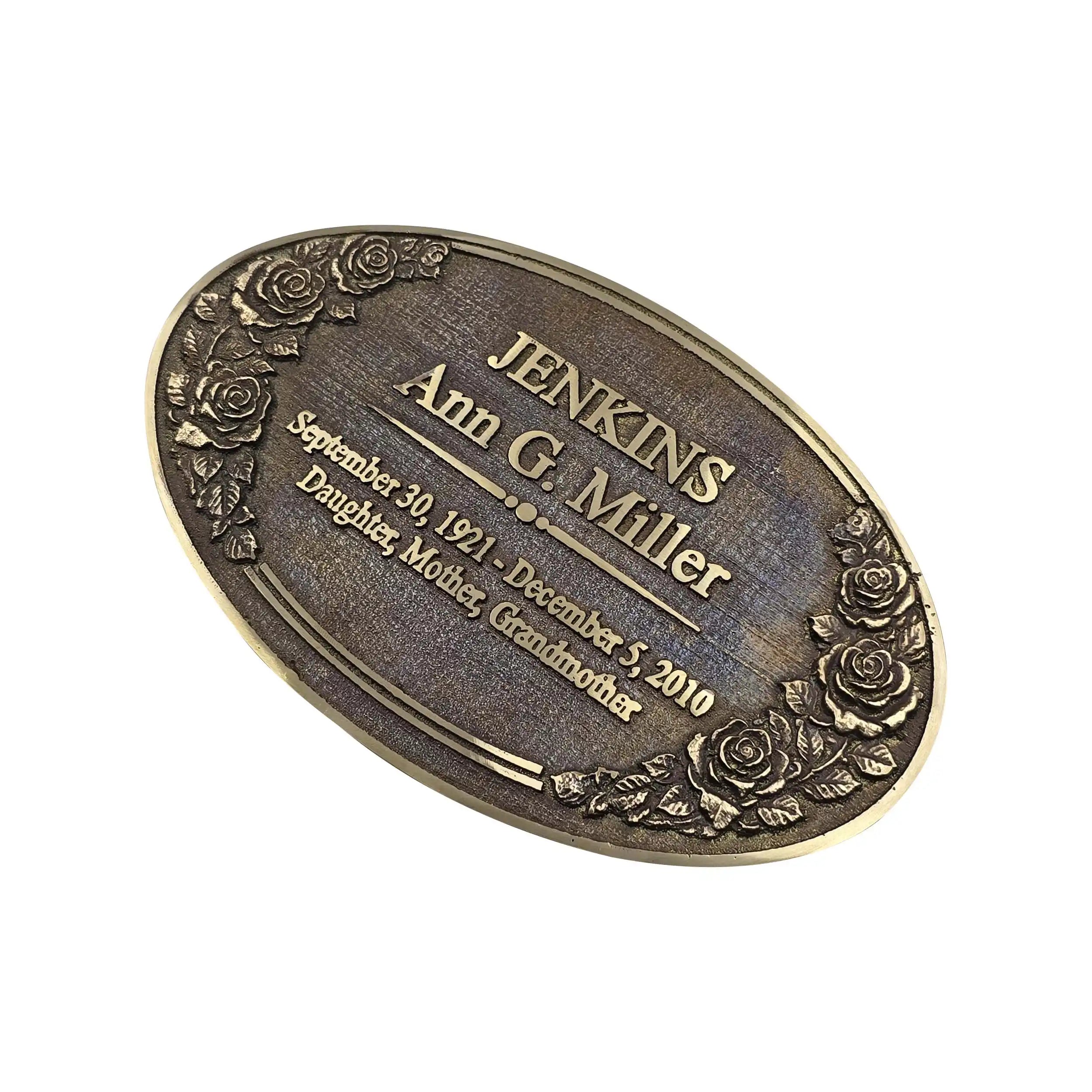 An oval bronze-toned metal keepsake plaque engraved with the name 'JENKINS Ann C. Miller' and dates, decorated with embossed floral rose designs around the border, shown on a plain white background.