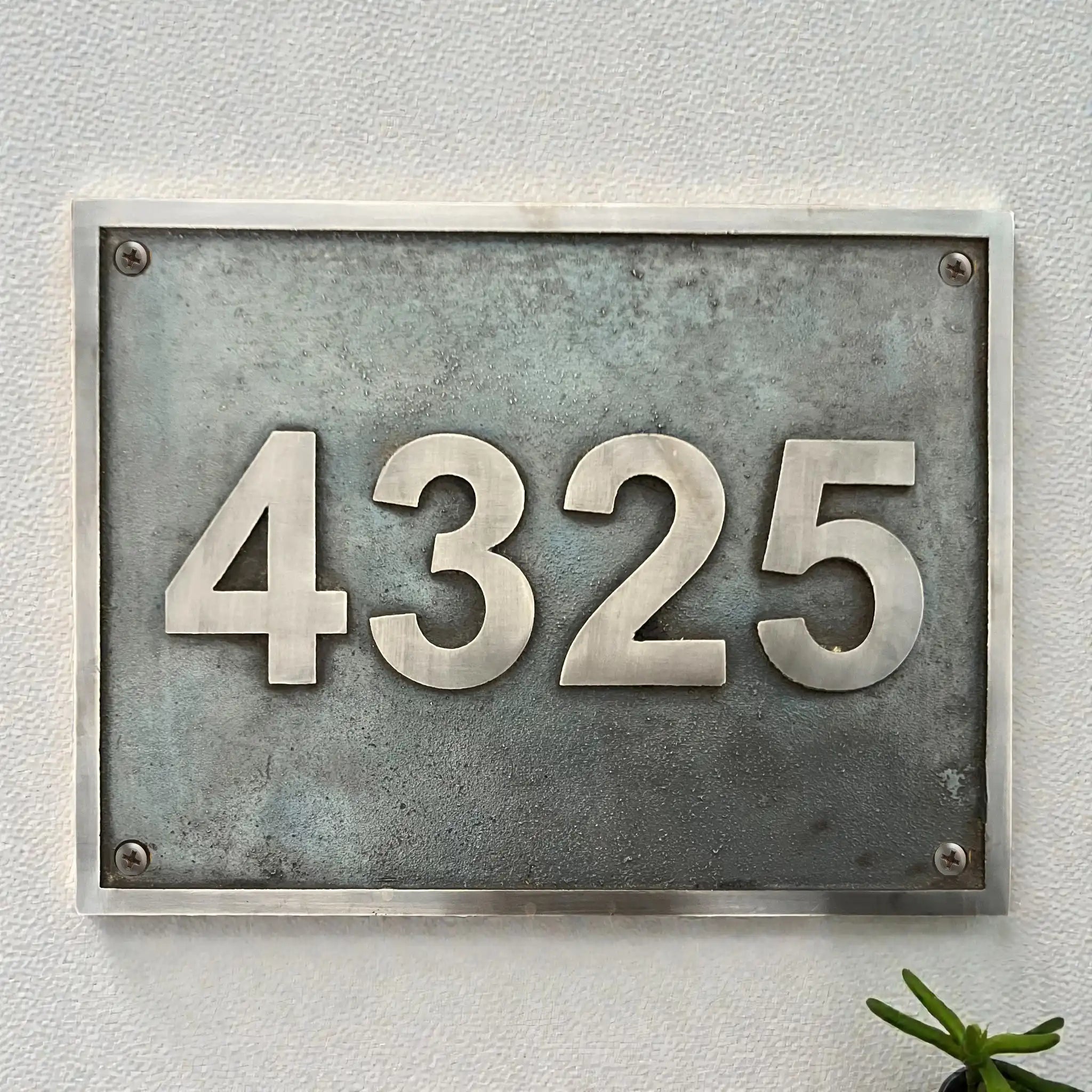 Metallic house number plate with '4325' on a light gray wall.