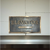 Bronze Address sign - Bronze 'ELEVATOR' sign with arrow on a textured wall.