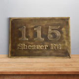 Brass house number sign with '115 Shearer Rd' on a wooden surface and light gray background