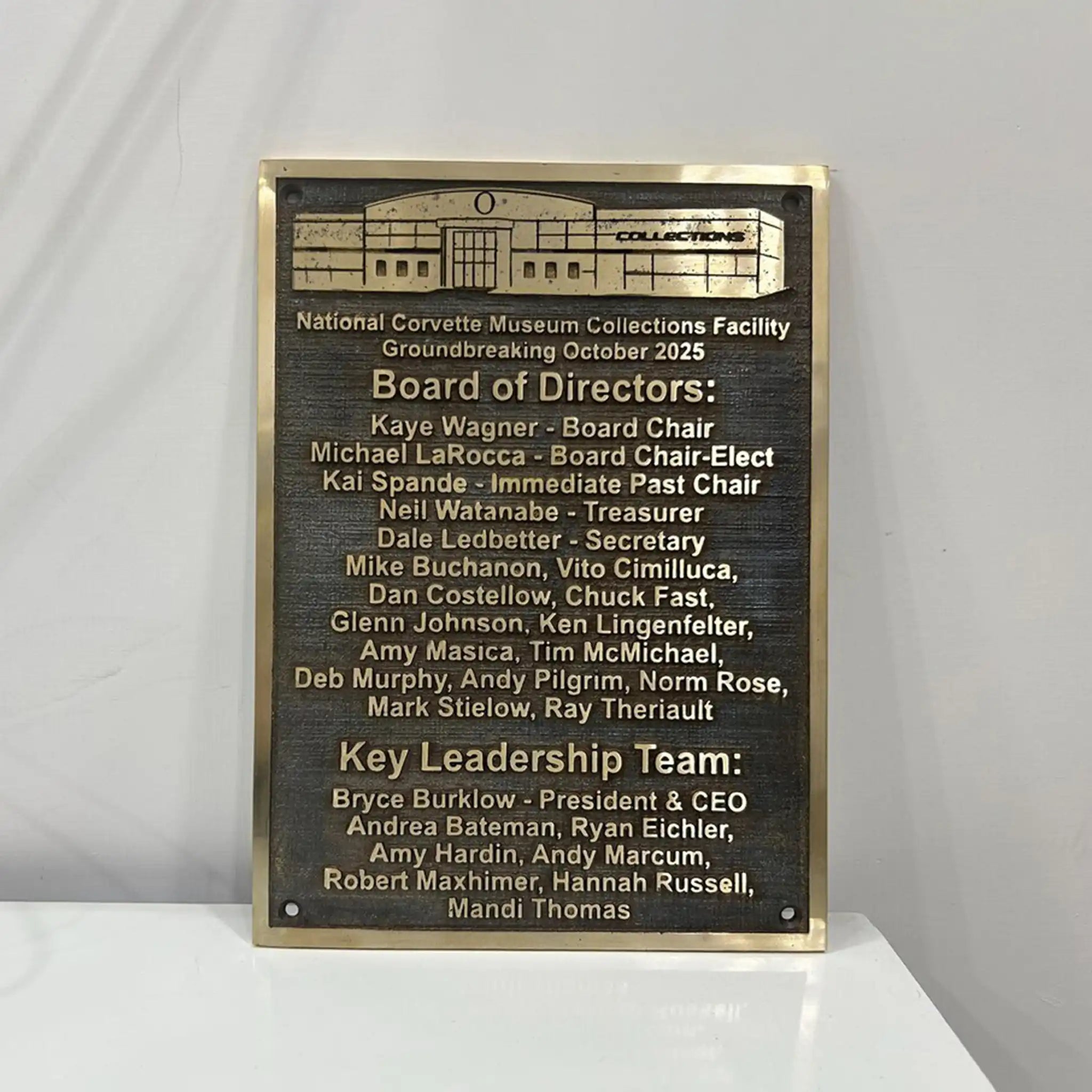 Bronze plaques for building with names and roles on a white surface and gray background