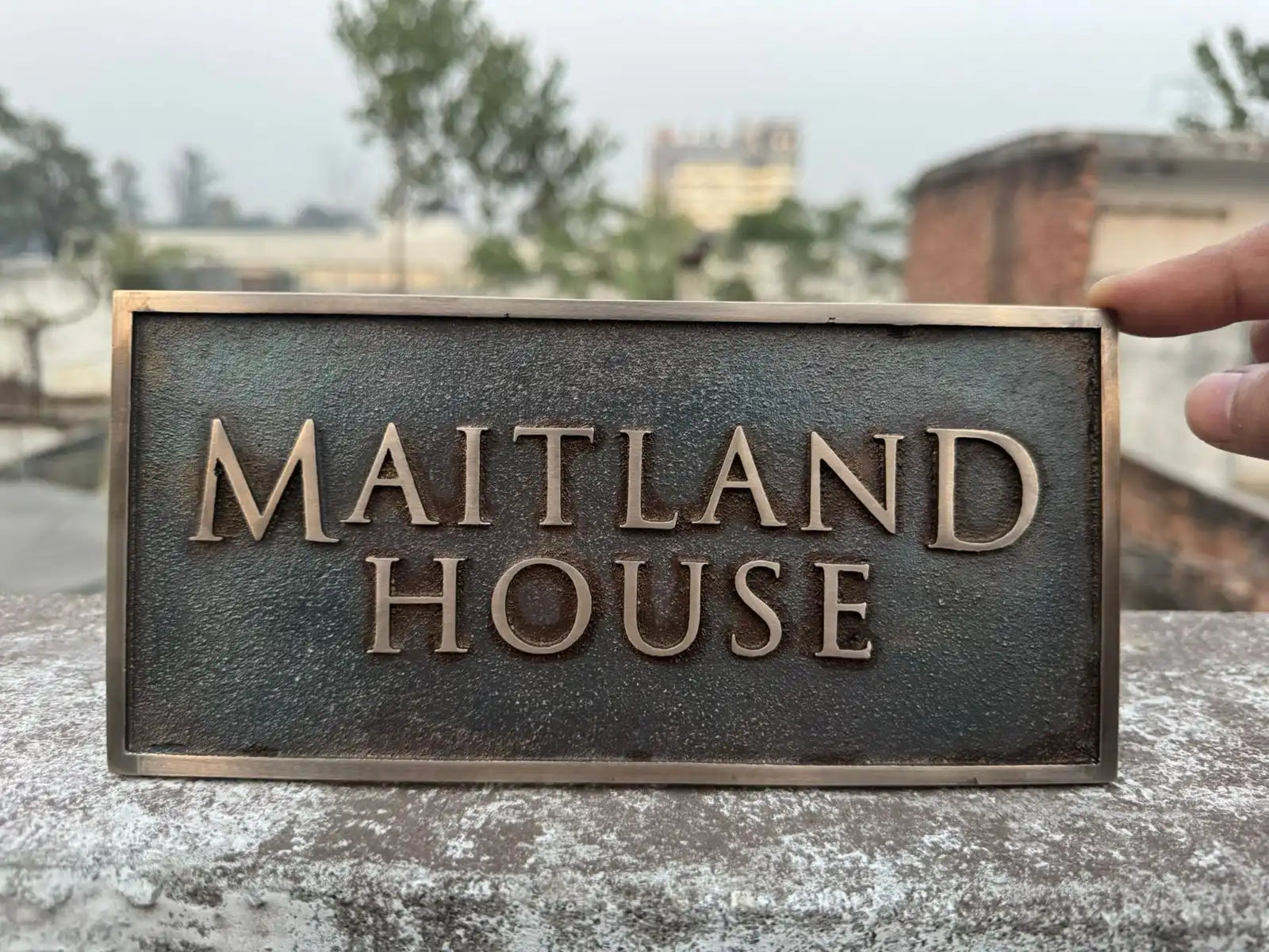 Bronze sign with 'Maitland House' text held against a blurred outdoor background
