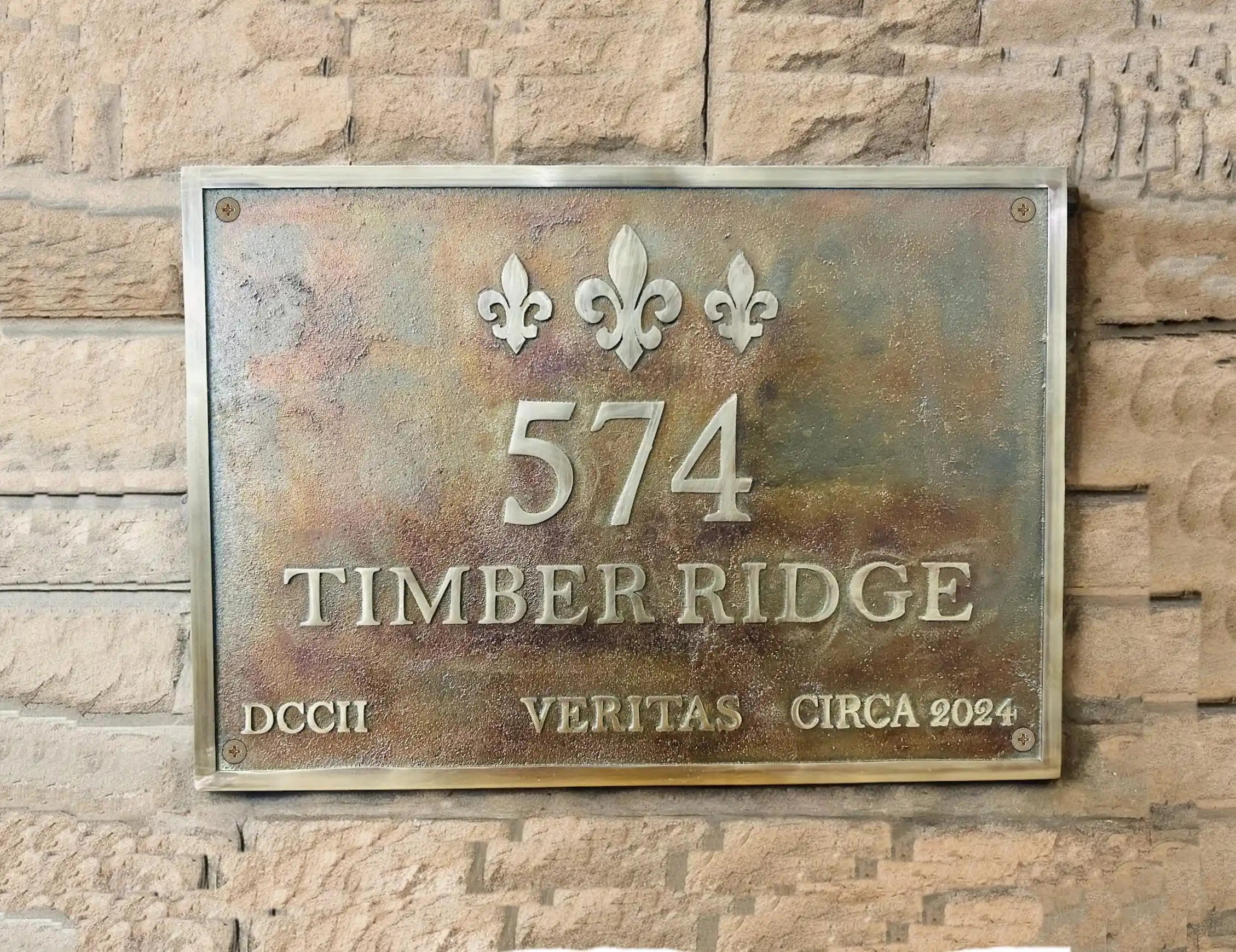Metallic house number sign with decorative elements on a stone wall.