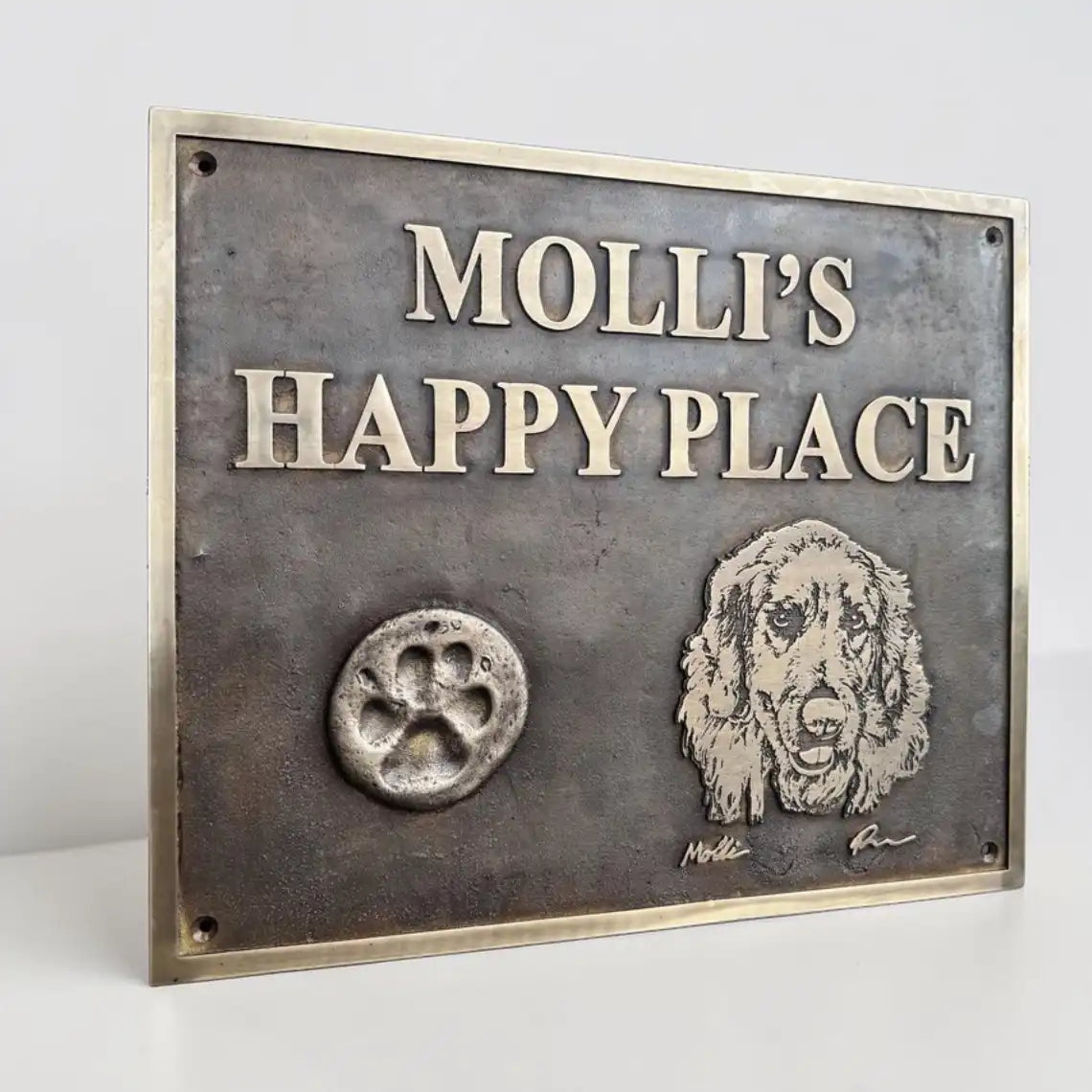Bronze sign with 'MOLLI'S HAPPY PLACE' text, paw print, and dog illustration on a metallic background.