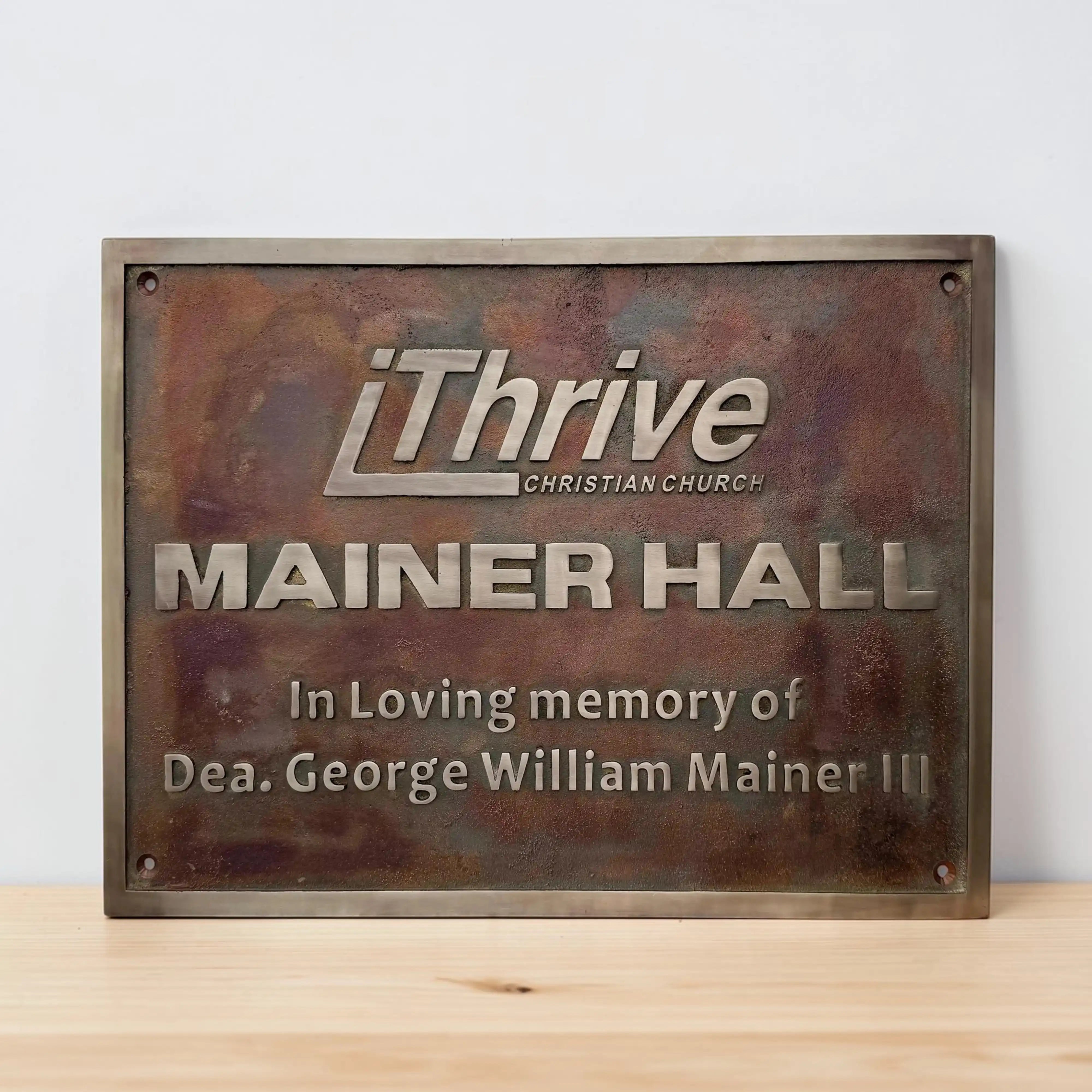 Bronze plaque with 'iThrive Christian Church' and 'Mainer Hall' text on a wooden surface.