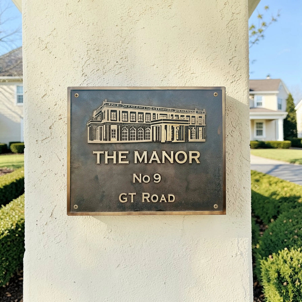 Bronze Plaque for 'The Manor No 9 GT Road' on a stone pillar with a residential background.