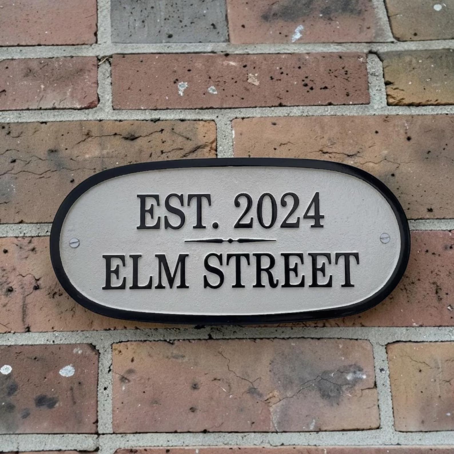 House number sign on a brick wall with 'EST. 2024 ELM STREET' text.