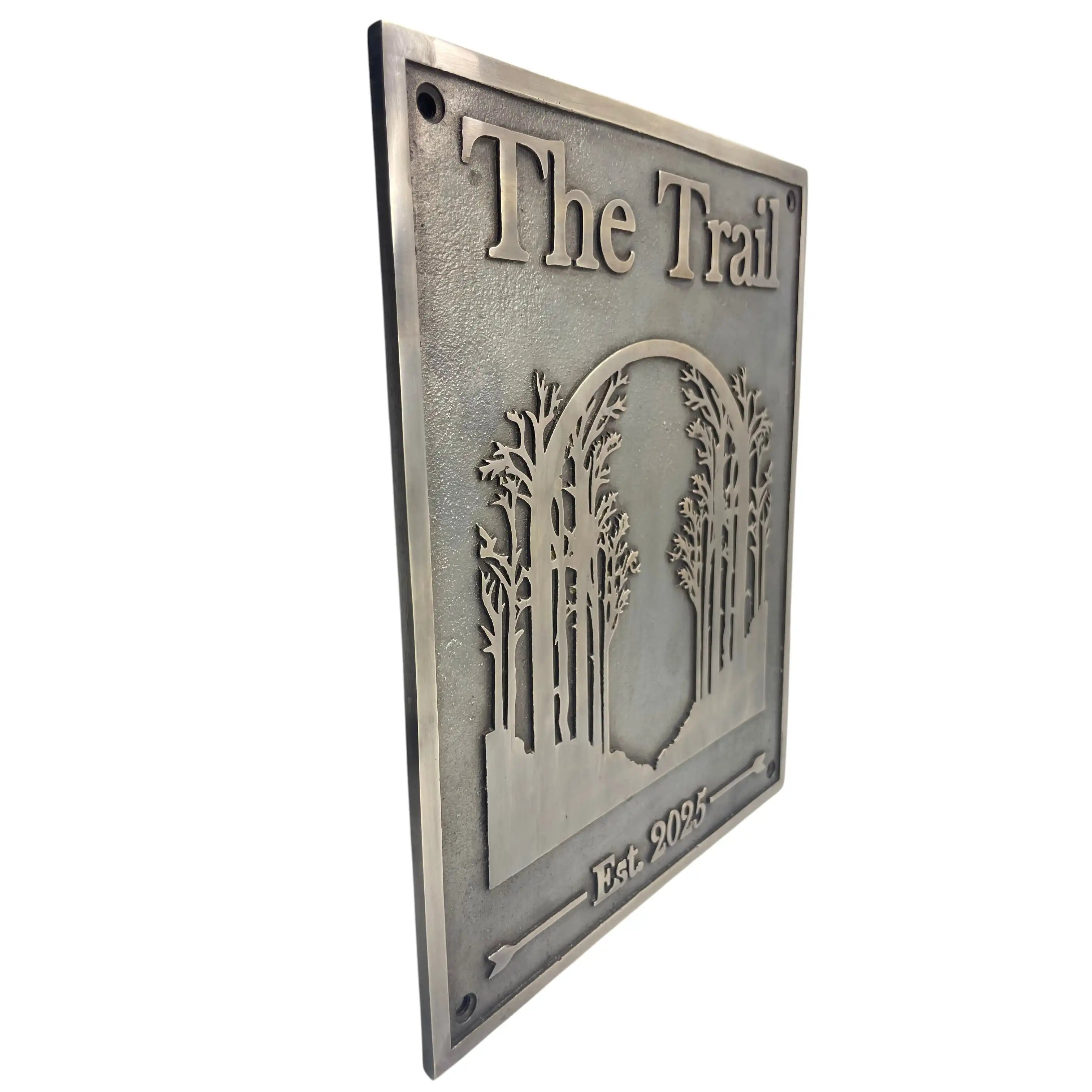 Bronze sign with 'The Trail' and tree design on a white background