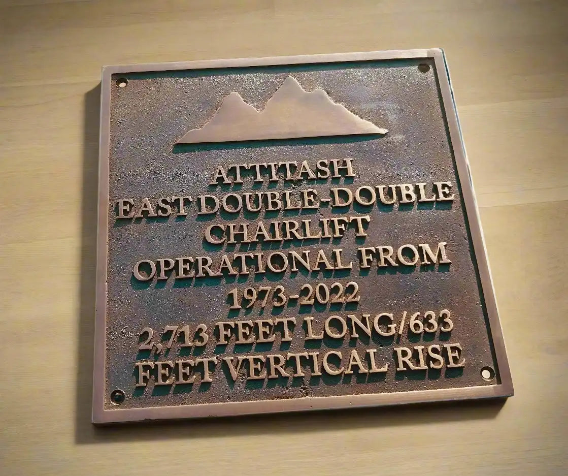 Metal plaque with engraved text about a chairlift on a wooden background