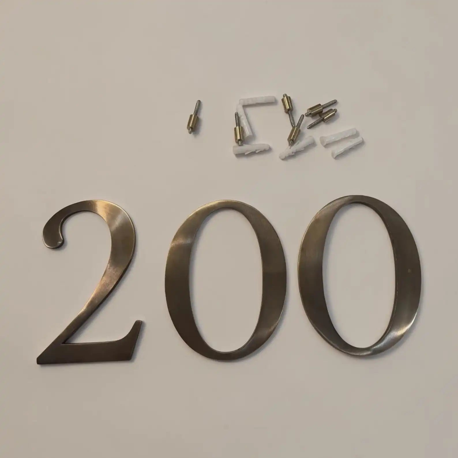 Metallic house number '200' in a brushed silver finish, shown with its mounting hardware on a plain light background.